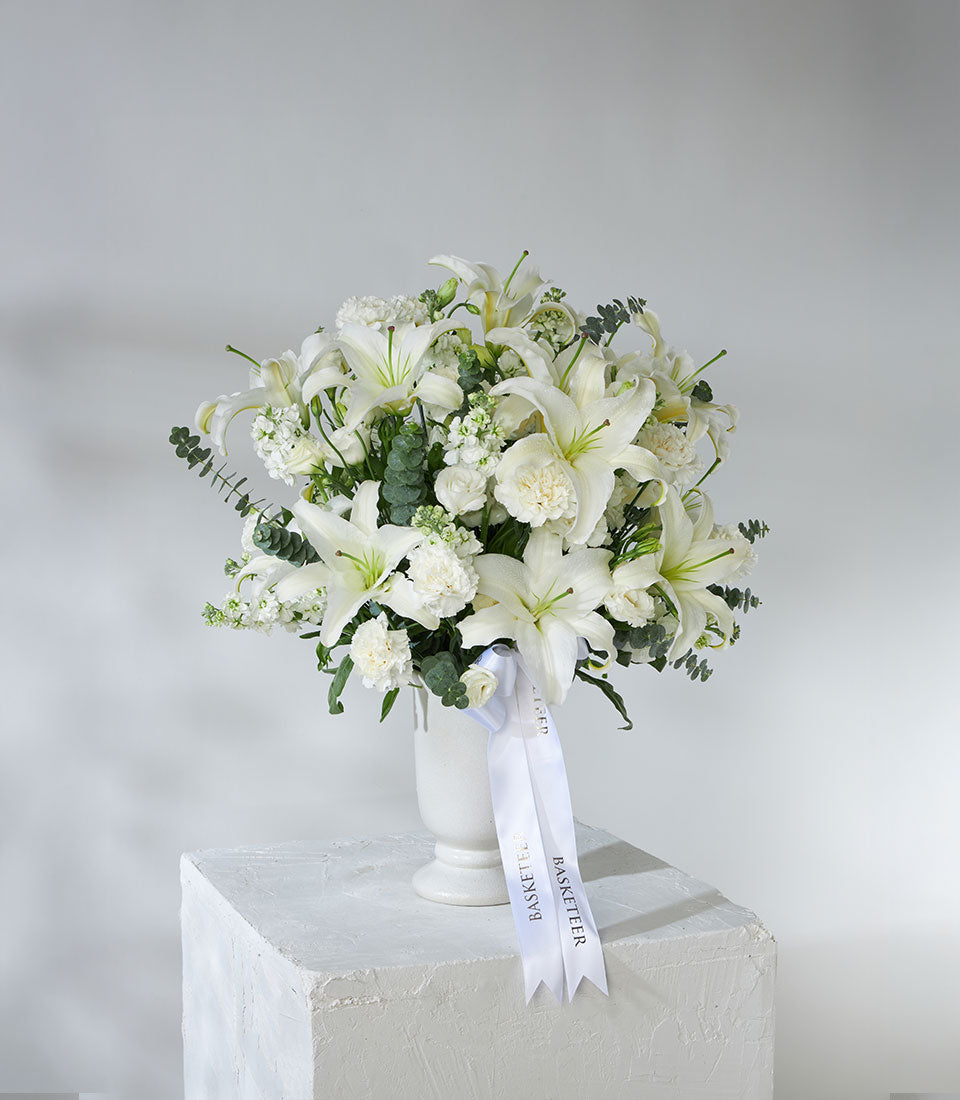 White lilies and carnations in elegant white vase with eucalyptus greenery, perfect luxury gift arrangement