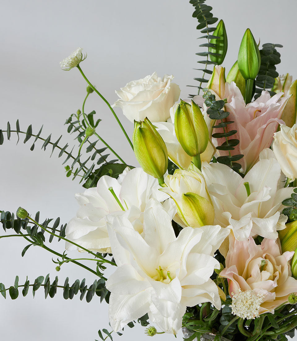 White roses and lilies with pale pink peonies in crystal wave glass vase