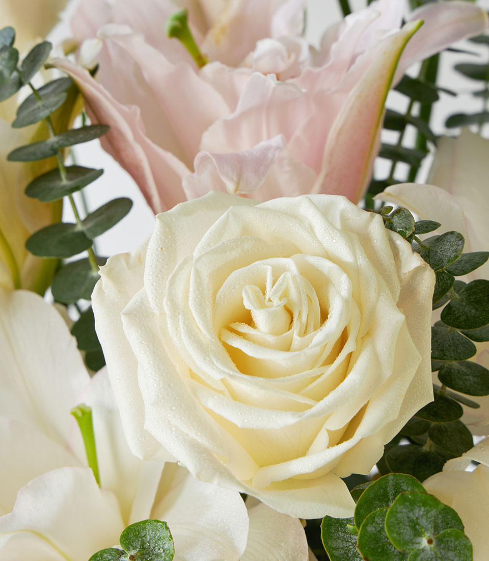 Creamy white roses and pink lilies with eucalyptus in crystal vase arrangement