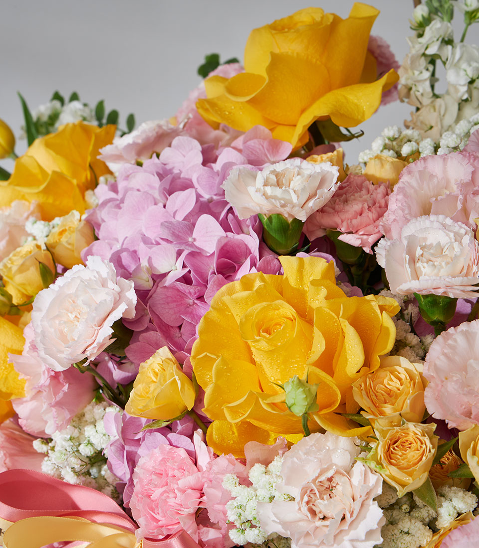 Bright yellow roses, pink hydrangeas and carnations in lush floral basket arrangement with pink ribbon