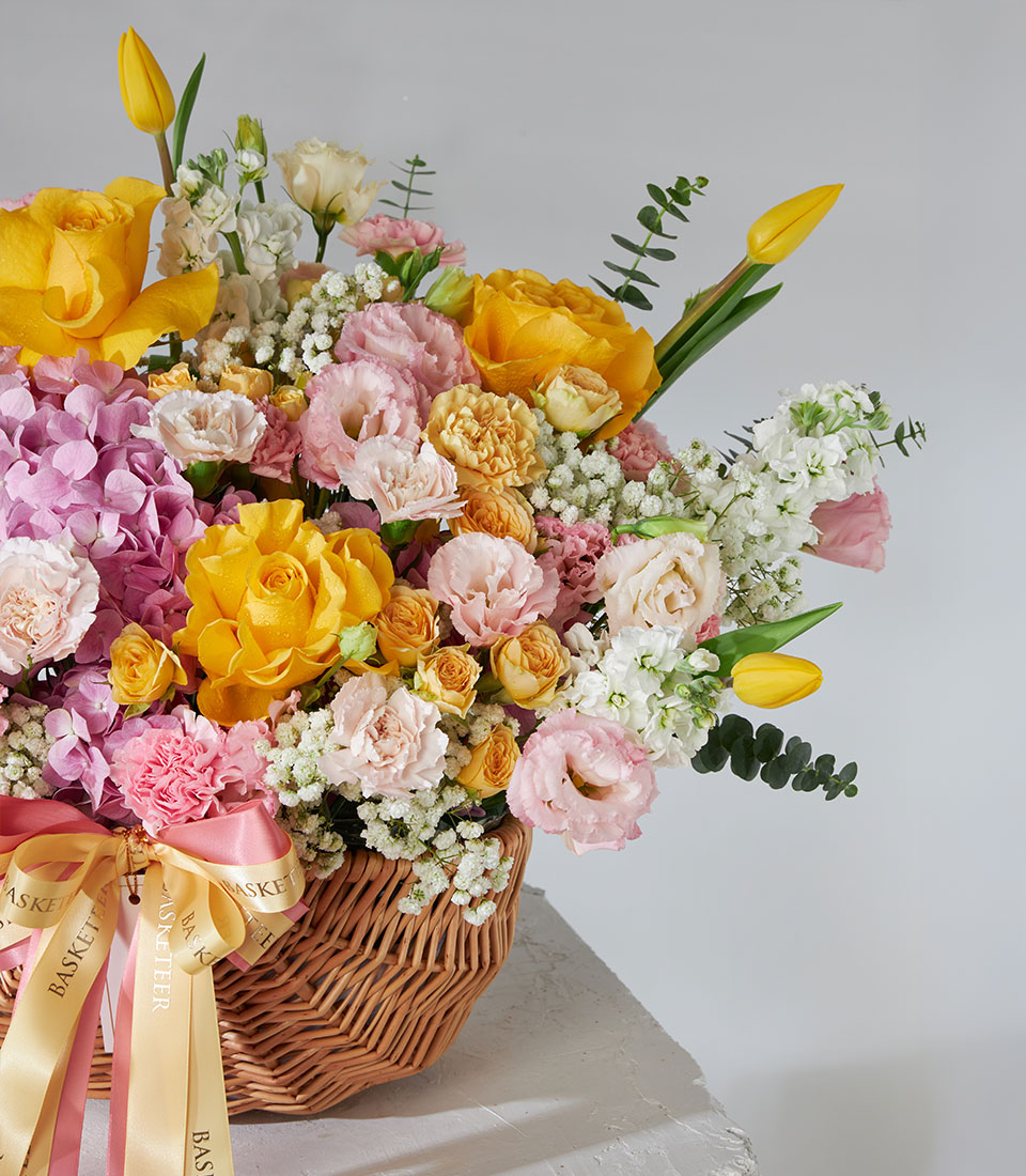 Vibrant yellow roses and pink hydrangea arrangement in woven basket with gold ribbon bow