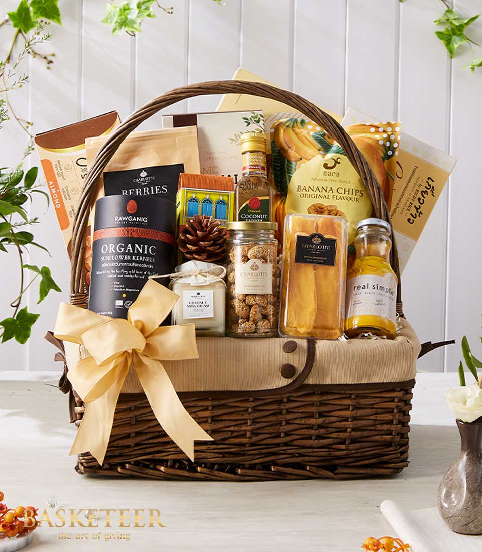 Woven wicker gift basket with gold ribbon bow filled with gourmet Thai snacks, organic kernels, coconut products, and banana