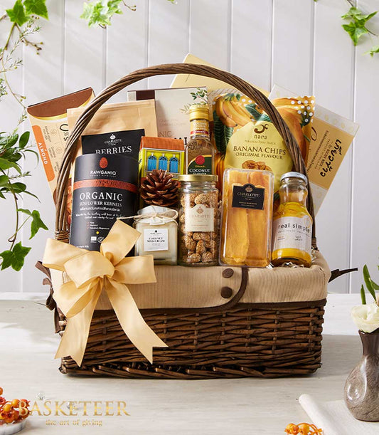 Woven wicker gift basket with gold ribbon bow filled with gourmet Thai snacks, organic kernels, coconut products, and banana
