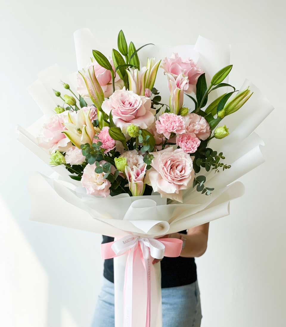 Pink roses and white lilies bouquet with eucalyptus, wrapped in white paper with ribbon bow