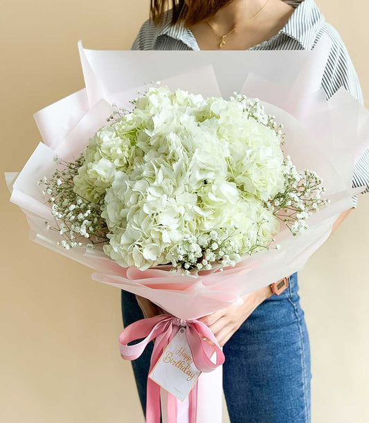 Elegant white hydrangea bouquet with baby's breath, pink ribbon and birthday tag