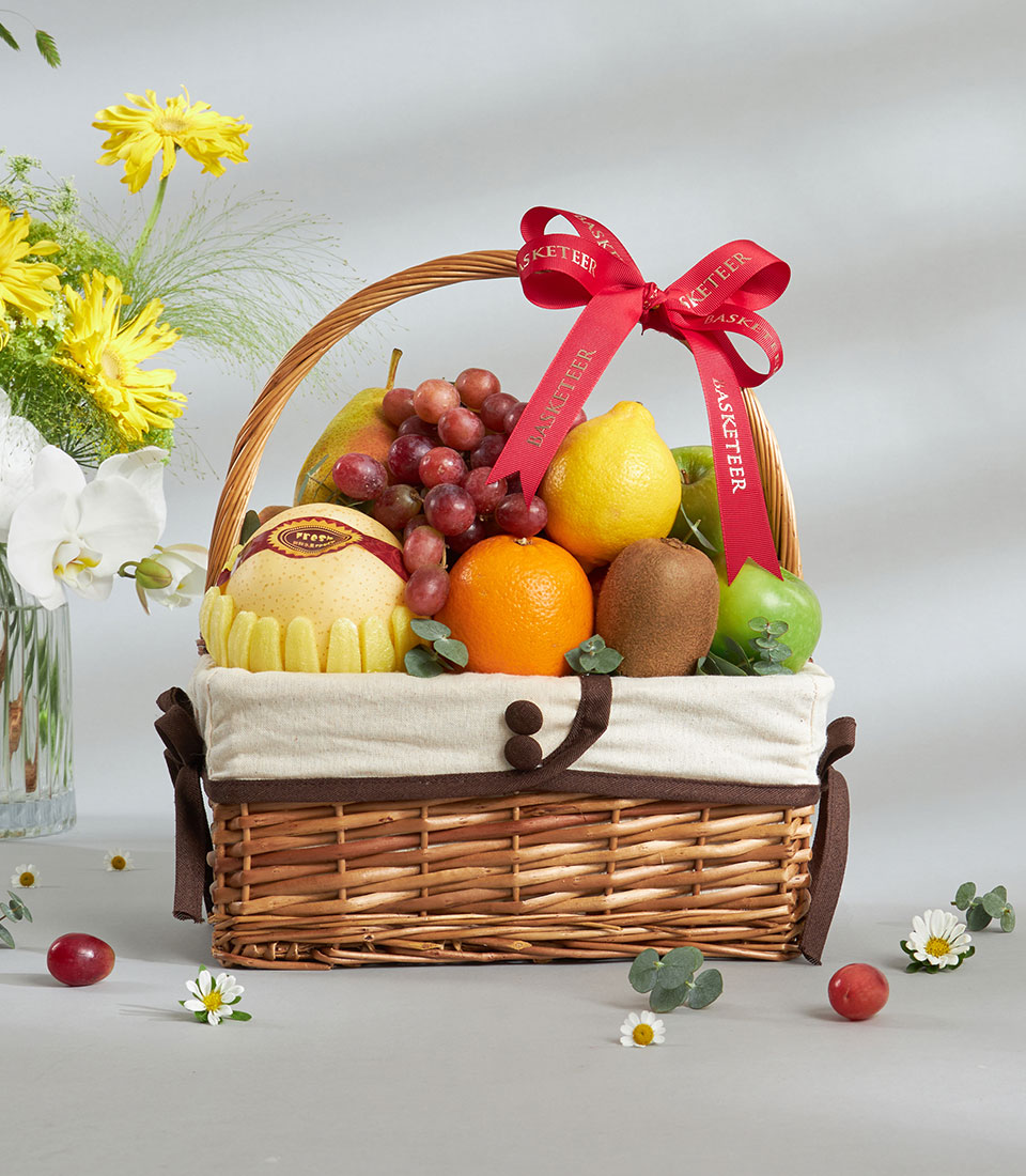Premium wicker fruit basket with red apples, pears, and seasonal produce, tied with gold-ribbon bow