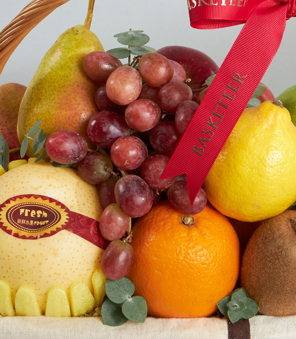 Premium imported fruit basket with red apples, pears, and fresh citrus in woven basket with ribbon