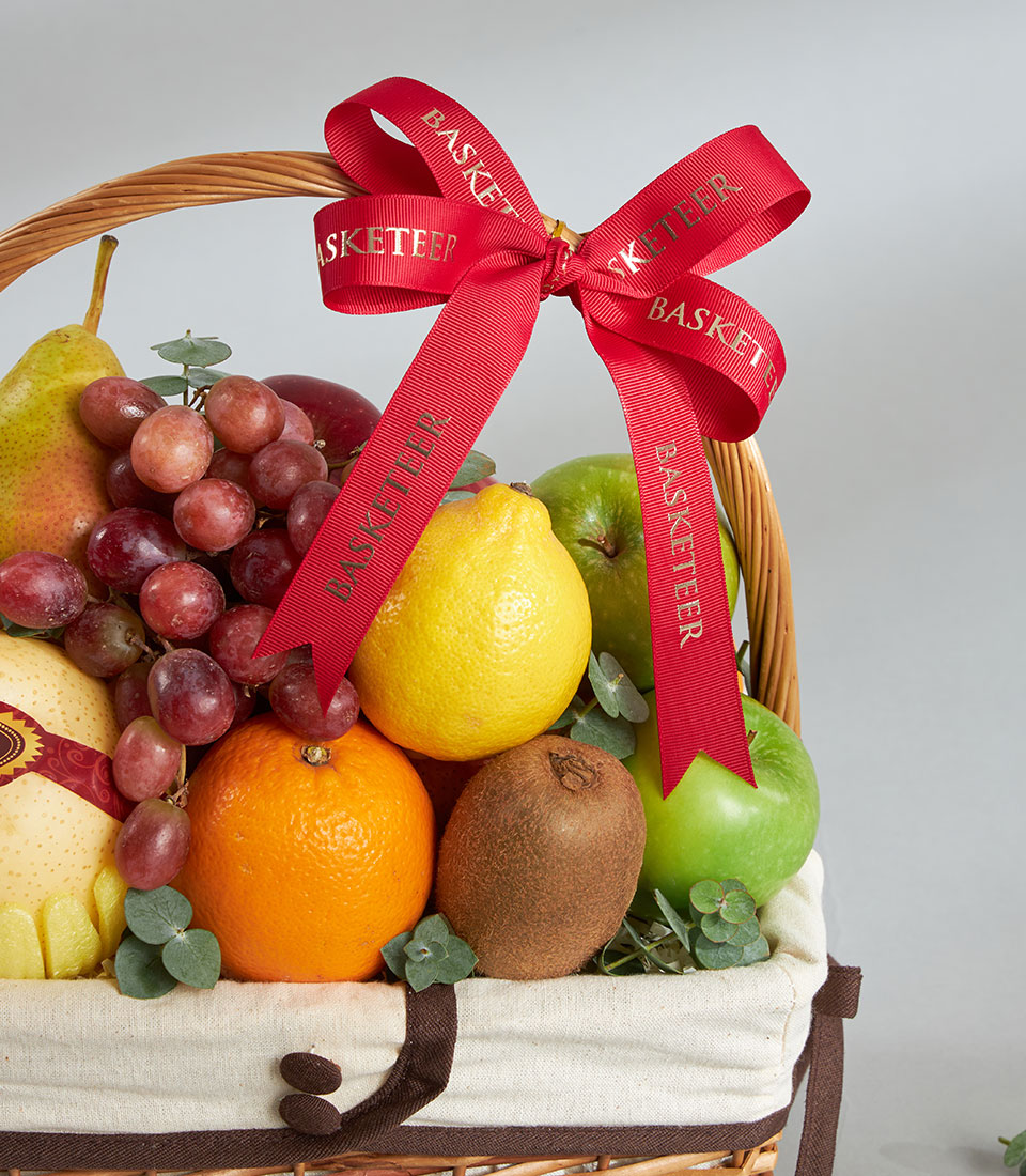 Premium wicker fruit basket with red apples, pears, grapes, and citrus, cream-lined with gold ribbon