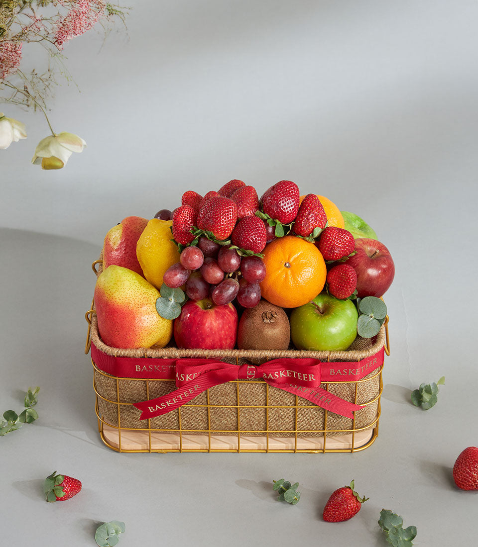 Gold wire fruit basket with strawberries, kiwi, apples, and citrus, tied with red ribbon