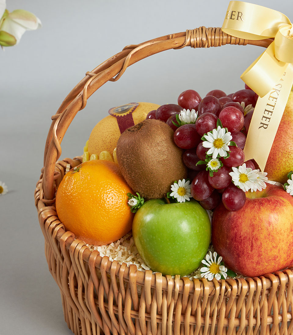 Luxury mixed fruit basket with imported apples, grapes, kiwi, and pear in woven wicker with white flowers and yellow ribbon