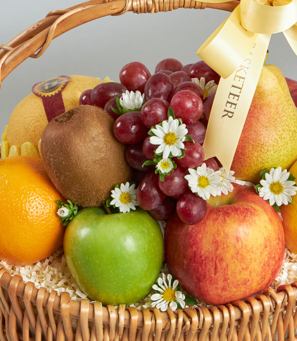 Luxury mixed fruit basket with red grapes, apples, pear, and kiwi in woven wicker with white ribbon
