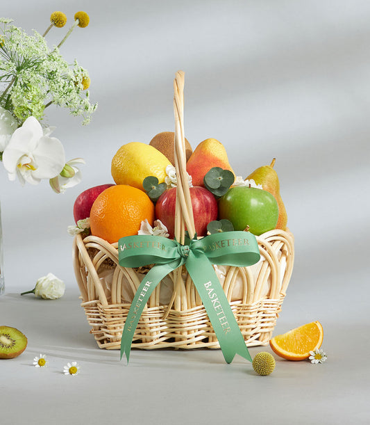 Classic fresh fruit basket with red and green apples, citrus, and kiwi in woven wicker with green ribbon