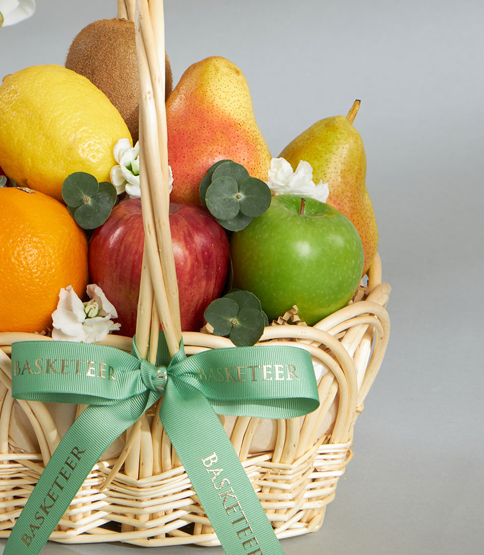 Classic woven wicker fruit basket with fresh imported oranges, apples, pears, kiwi, lemon, white flowers and eucalyptus