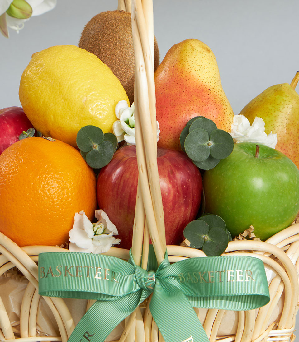 Wicker fruit basket with fresh lemons, oranges, apples, pears, kiwis and eucalyptus greenery, tied with green ribbon