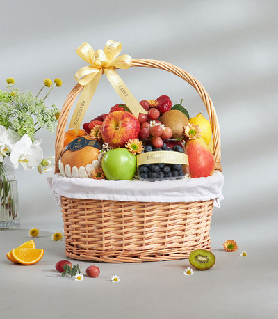 Luxury mixed imported fruit basket with apples, grapes, strawberries, kiwi, and pears in wicker with yellow ribbon