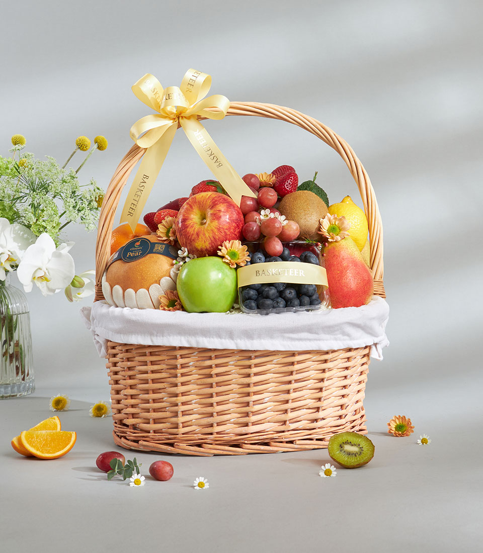 Luxury mixed imported fruit basket with apples, grapes, strawberries, kiwi, and pears in wicker with yellow ribbon