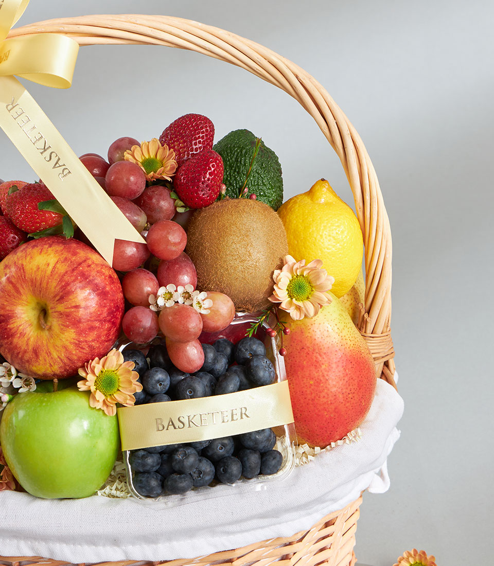 Woven wicker fruit basket with fresh apples, grapes, strawberries, kiwi, and berries tied with cream ribbon