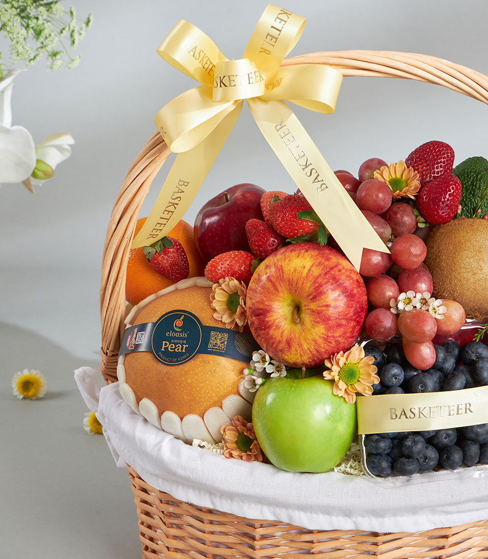 Woven wicker luxury fruit basket with fresh apples, grapes, berries, and imported pears, accented with delicate florals