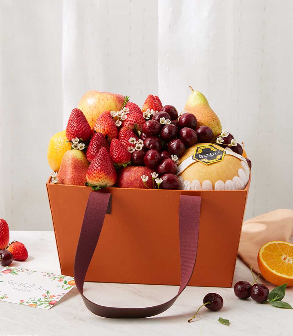 Premium fresh fruit gift basket with strawberries, cherries, apples and pears in orange paper bag with fabric handles