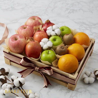 Wooden fruit basket with red and green apples, pomegranates, kiwis, oranges, and cotton stems, tied with brown and burgundy