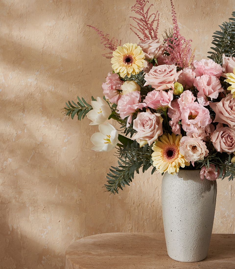 Pastel pink roses, yellow gerberas, and white tulips in grey ceramic vase