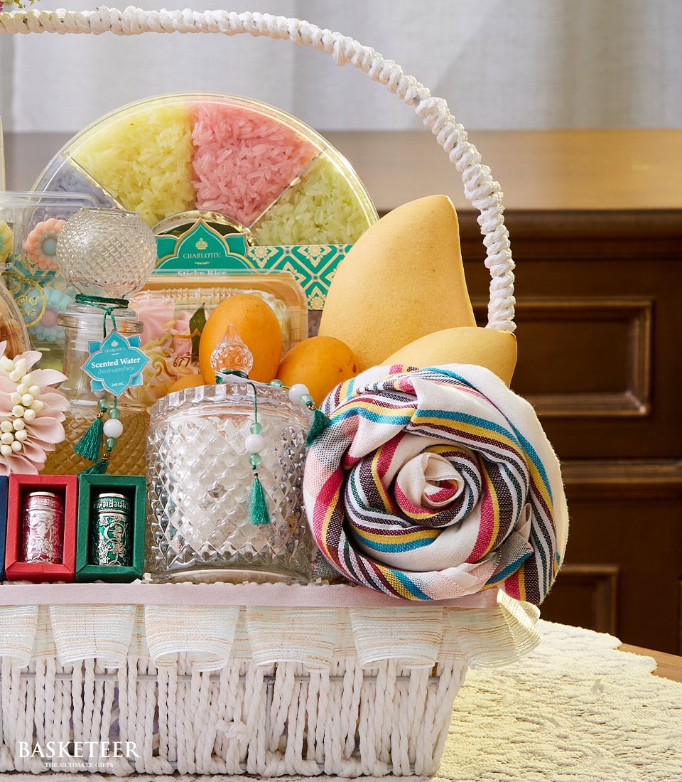 White woven gift basket with colorful sticky rice, fresh mangoes, mandarins, scented candles, and Thai silk for Songkran New