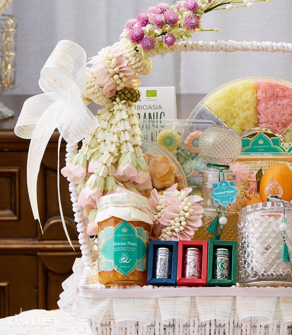 White woven gift basket with white bow and fresh white and pink flower garland, filled with Thai Songkran treats, jam,