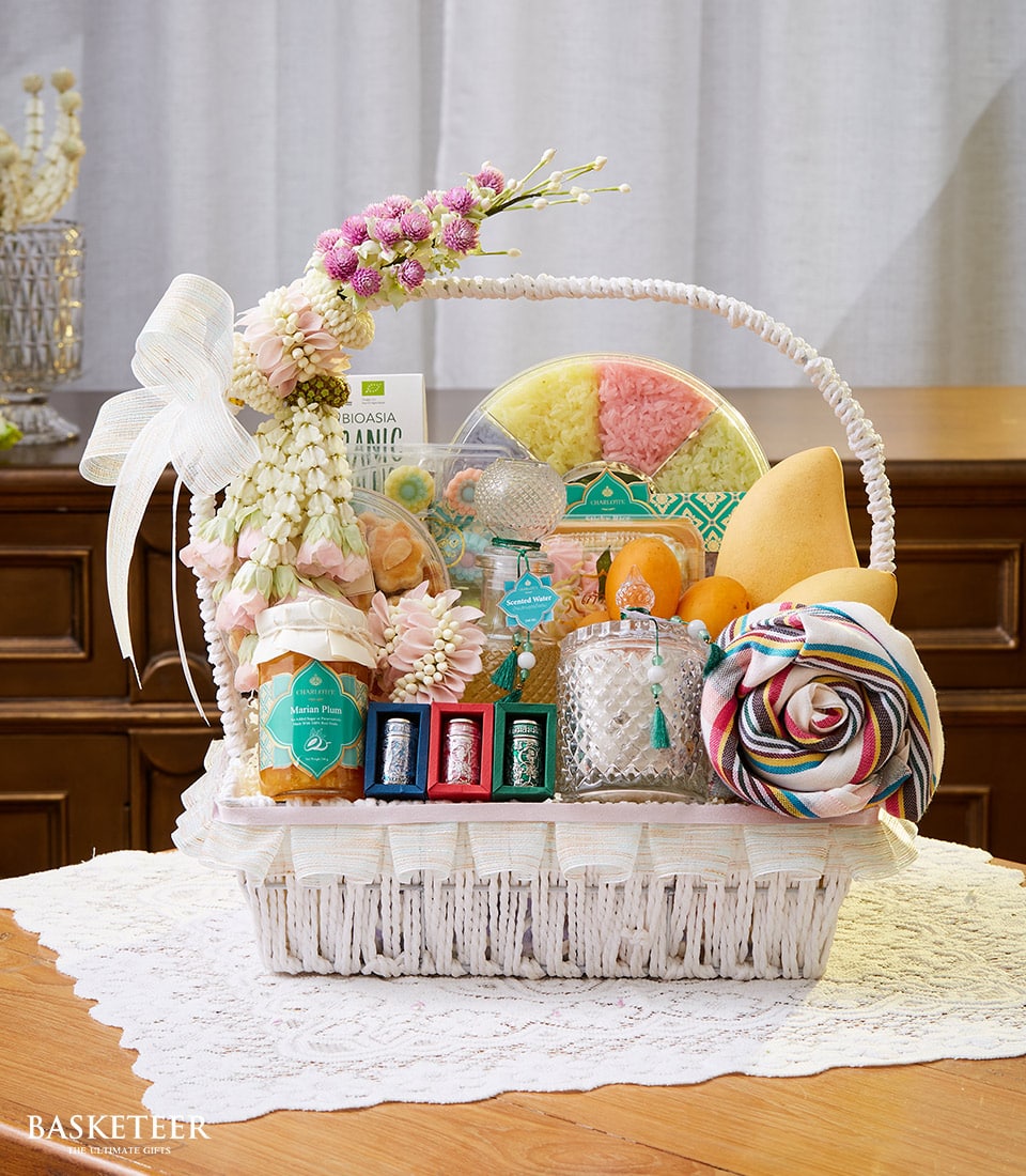 White woven gift basket with pink and white floral garland, filled with Thai treats, fresh mangoes, and Songkran scented