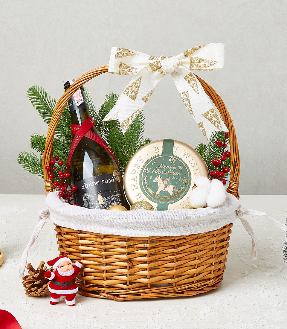 Festive wicker Christmas wine gift basket with Alpine Road bottle, green tin, pine branches, berries, and holiday ribbon