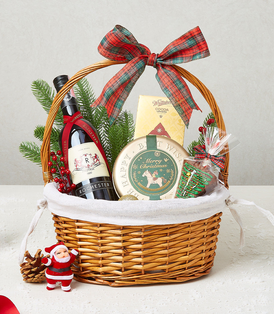 Woven wicker Christmas wine basket with red wine, festive treats, and plaid bow