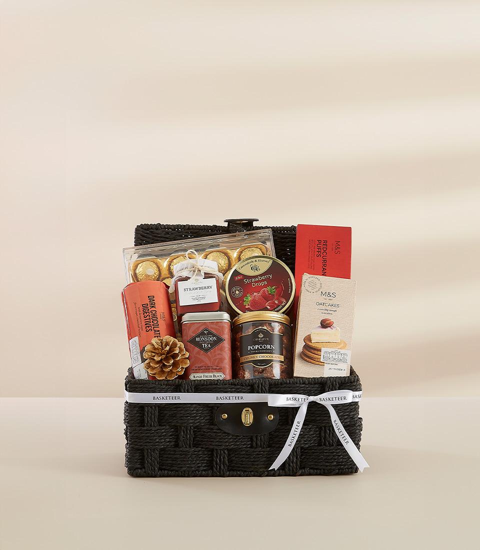 Black woven gourmet hamper with chocolates, jam, tea, and artisan treats tied with white ribbon, ideal for New Year gifting