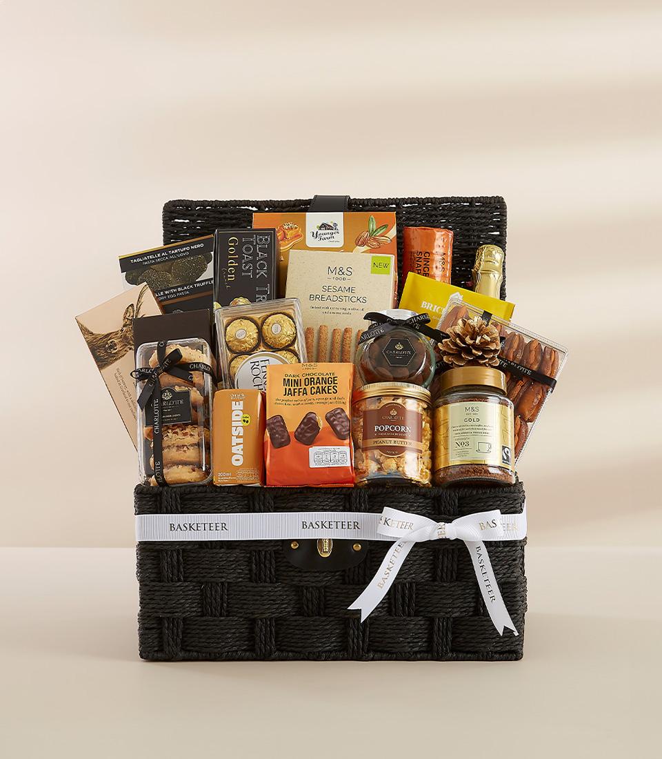 Elegant black wicker gourmet hamper with white ribbon bow, filled with premium snacks, chocolates, and sparkling beverage