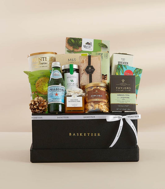 Premium gourmet gift hamper with sparkling water, preserves, tea, and crackers in black box with white ribbon