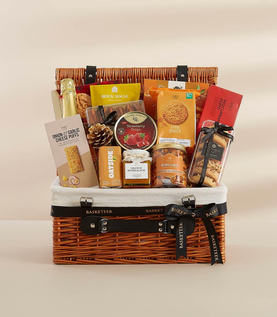 Woven wicker gift hamper with gourmet treats, sparkling wine, and artisan snacks in warm gold and orange tones for New Year