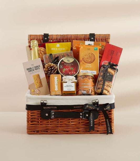 Woven wicker gift hamper with gourmet treats, sparkling wine, and artisan snacks in warm gold and orange tones for New Year