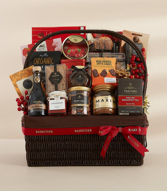 Premium gourmet gift basket with chocolate, tea, preserves, and festive red ribbon on dark woven wicker