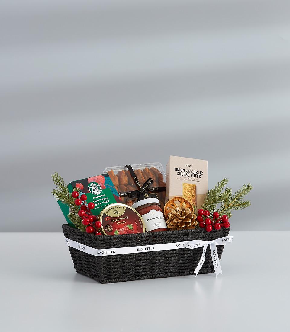 Luxe dark woven gift basket filled with gourmet treats, strawberry jam, cheese puffs, and festive greenery for New Year