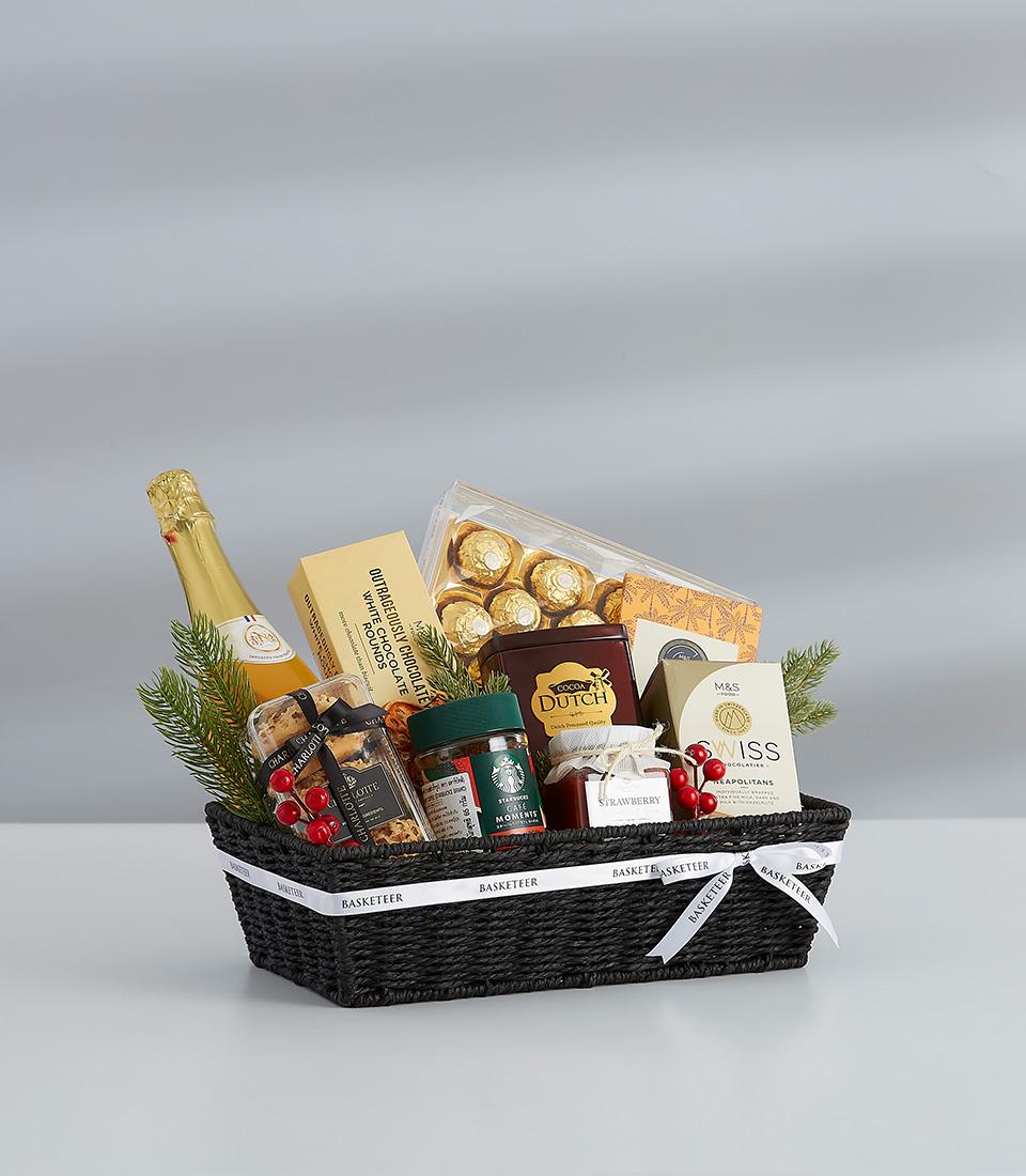 Dark woven gift basket with champagne, gourmet chocolates, jam, and festive greenery for New Year celebrations
