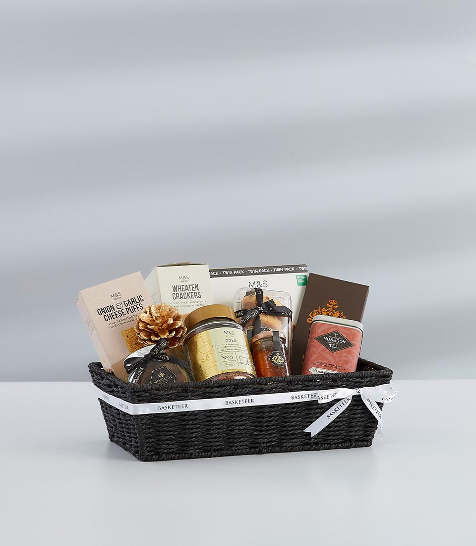 Black woven gift basket with winter gourmet selection, white ribbon bow, and gold pinecone for New Year celebrations
