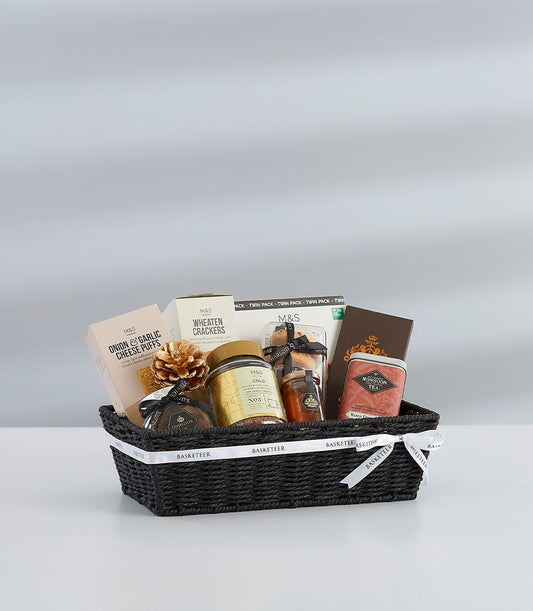Black woven gift basket with winter gourmet selection, white ribbon bow, and gold pinecone for New Year celebrations