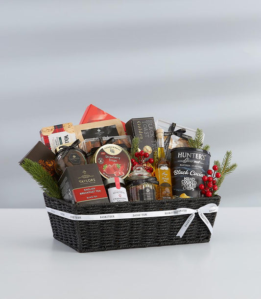 Dark woven gift basket filled with gourmet tea, caviar chips, truffle toast, and festive trimmings, tied with white