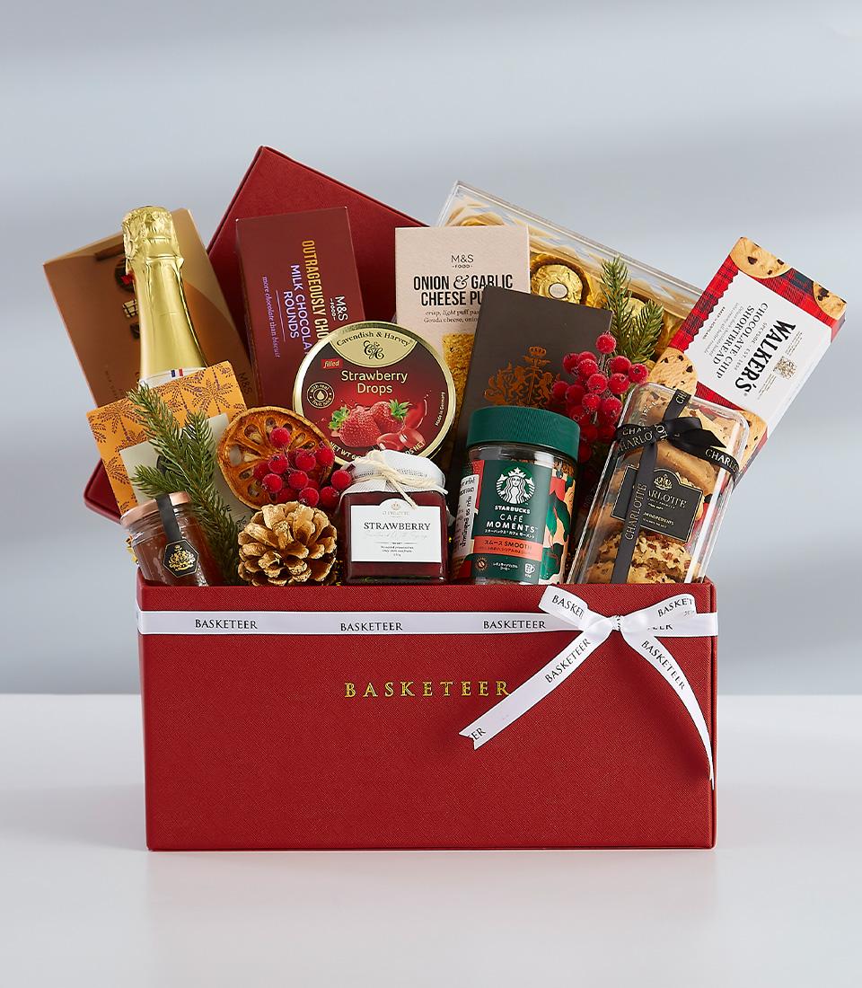 Festive red leather gift hamper with gourmet treats, sparkling wine, and holiday greenery