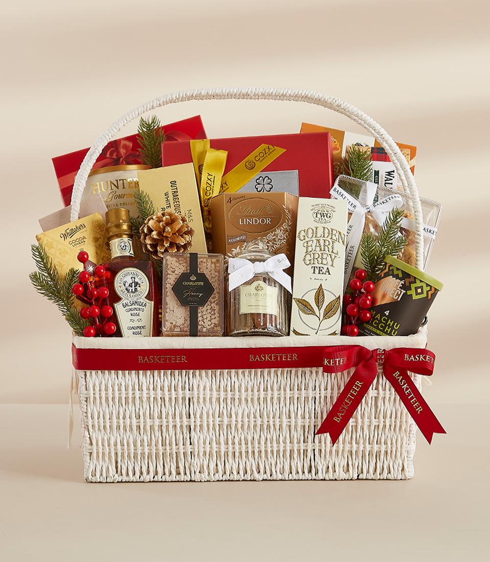 White woven luxury gift basket filled with gourmet chocolates, tea, balsamic vinegar, and festive holiday treats tied with
