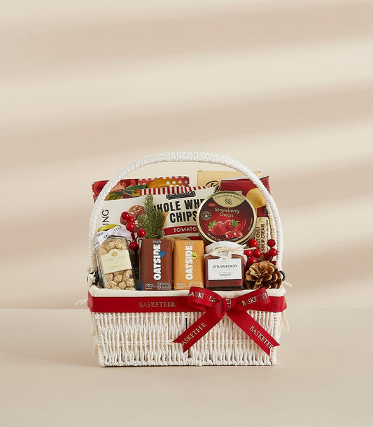 White woven gift basket filled with gourmet snacks, strawberry jam, and festive holiday treats tied with red bow