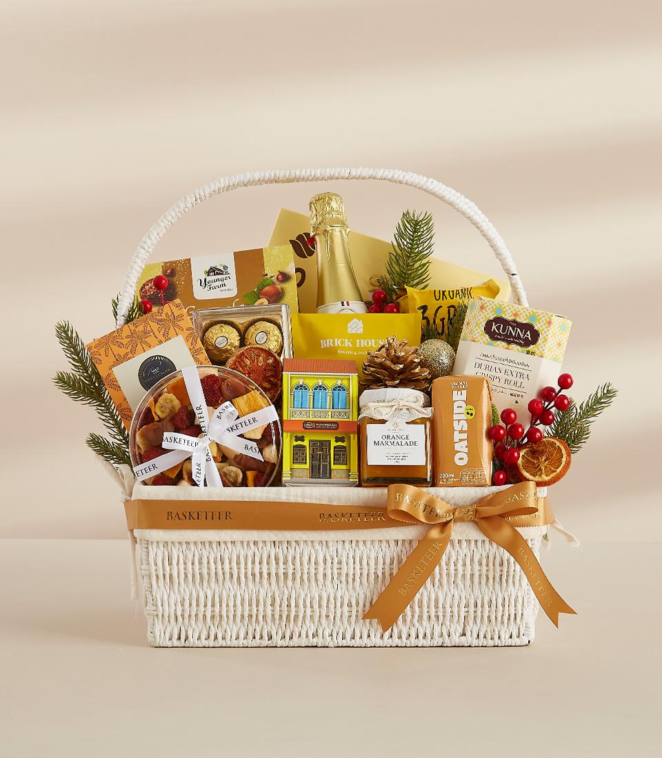 White woven luxury gift basket with gold ribbon, gourmet treats, champagne, and festive pine accents for New Year