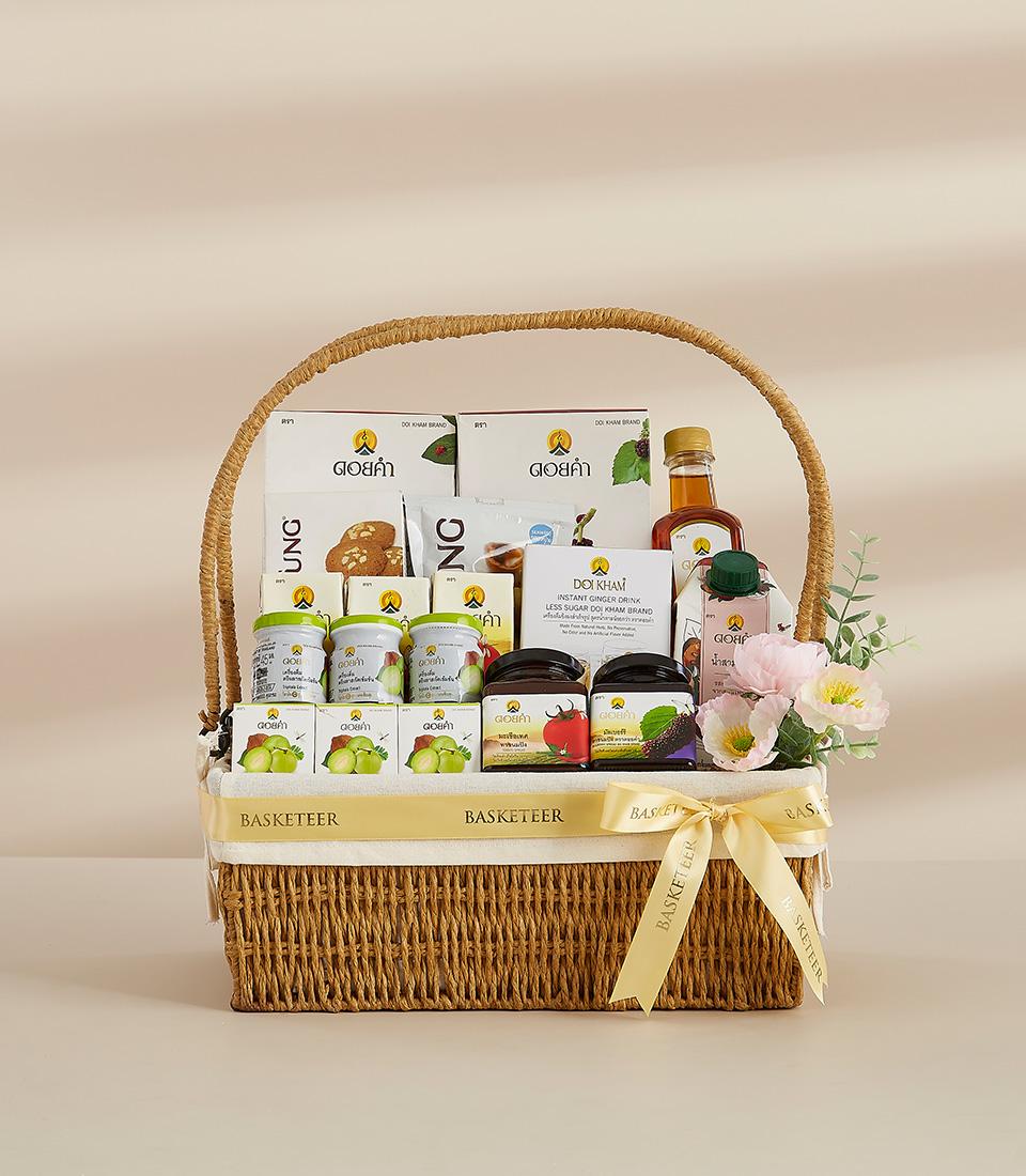 Woven wicker gift basket with gourmet preserves, ginger drink mix, cookies, and fresh flowers, tied with yellow Basketeer