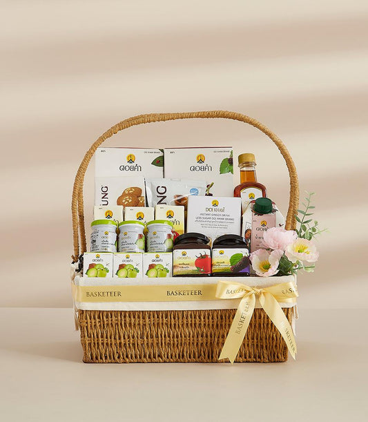 Woven wicker gift basket with gourmet preserves, ginger drink mix, cookies, and fresh flowers, tied with yellow Basketeer