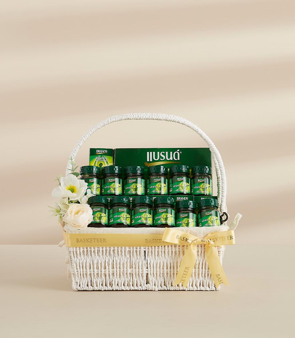 Premium herbal essence gift basket with dark glass bottles, white flowers, and golden Basketeer ribbon