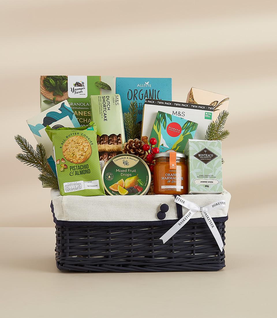 Dark wicker gift basket with gourmet New Year treats, pistachios, shortcake, marmalade, and jasmine tea with festive greenery
