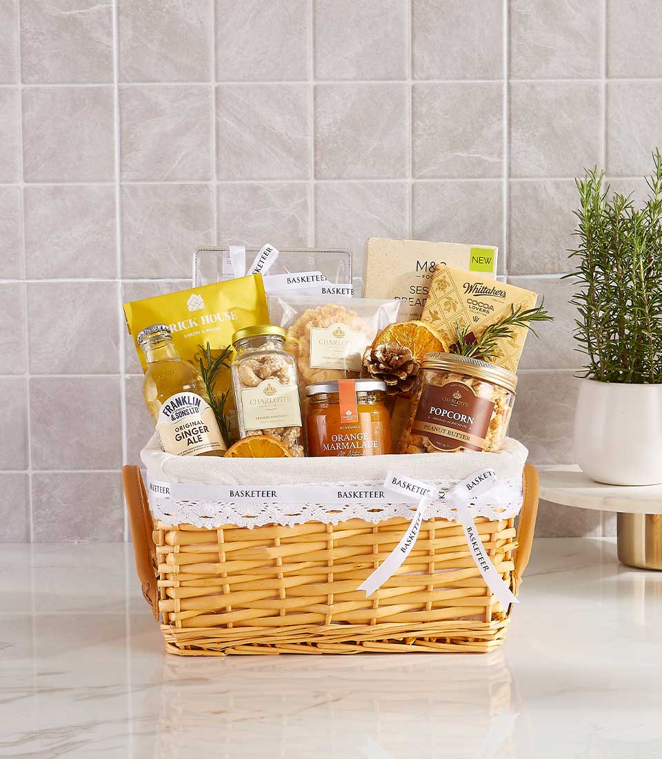 Light brown wicker gift basket with gourmet treats, ginger ale, marmalade, and cashews tied with white ribbon for New Year